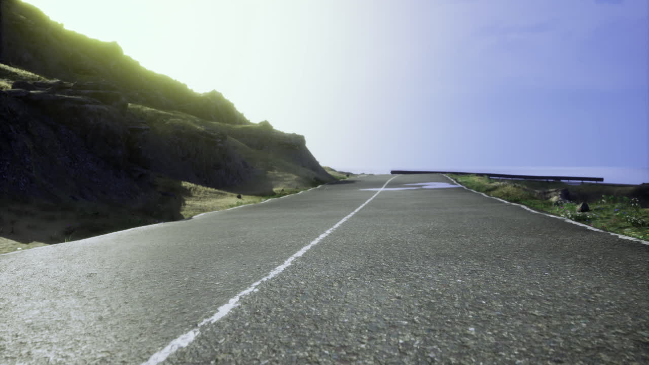 Winding coastal road under bright sky near rocky cliff at sunset
