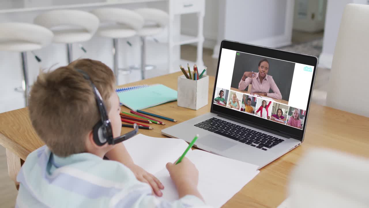 Schoolboy using laptop for online lesson at home, with diverse teacher and class on screen