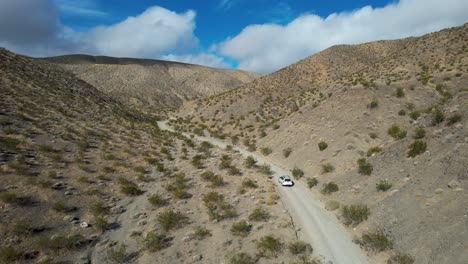 Coche-Blanco-Conduciendo-Por-La-Carretera-Del-Valle-Del-Desierto-Con-Cielo-Azul,-Vista-Aérea