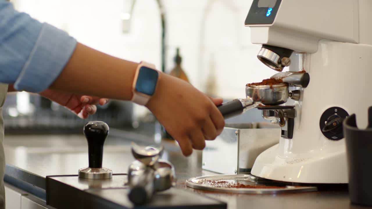 Donna afroamericana che sblocca un portafiltro e avvia un macinino per l'espresso al bancone di un bar