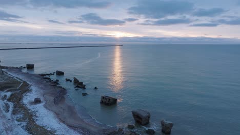 beautiful aerial establishing view of karosta concrete coast fortification ruins, vibrant high contrast sunset over calm baltic sea, winter evening, wide drone shot moving forward high