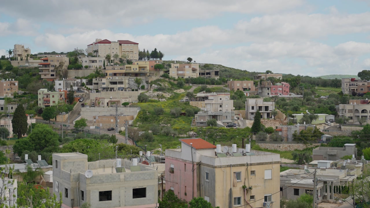 Arabic town or village in Northern Israel during spring time. Wide shot of houses and small streets or Christian and Muslim community living together. Peaceful green hills and blue cloudy sky