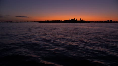 wide shot, from a boat, showing sailing ship, statue of liberty at dusk, teal and orange sky