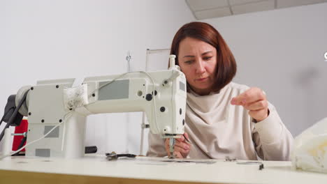 Fashion designer cleans dirt around needle part of sewing machine, picks up screwdriver to loosen nut in workshop environment, focusing on maintenance for smooth operation and thorough performance