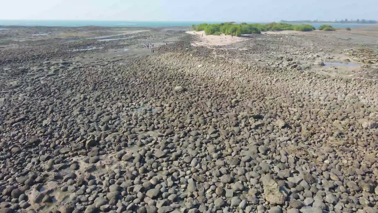Shallow water created a natural rocky beach with a few tourists exploring the island. Aerial footage - Seascape, natural beach, tide concept