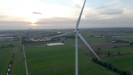 Spinning-windmill-blades-in-a-rural-area-and-industry-in-the-background