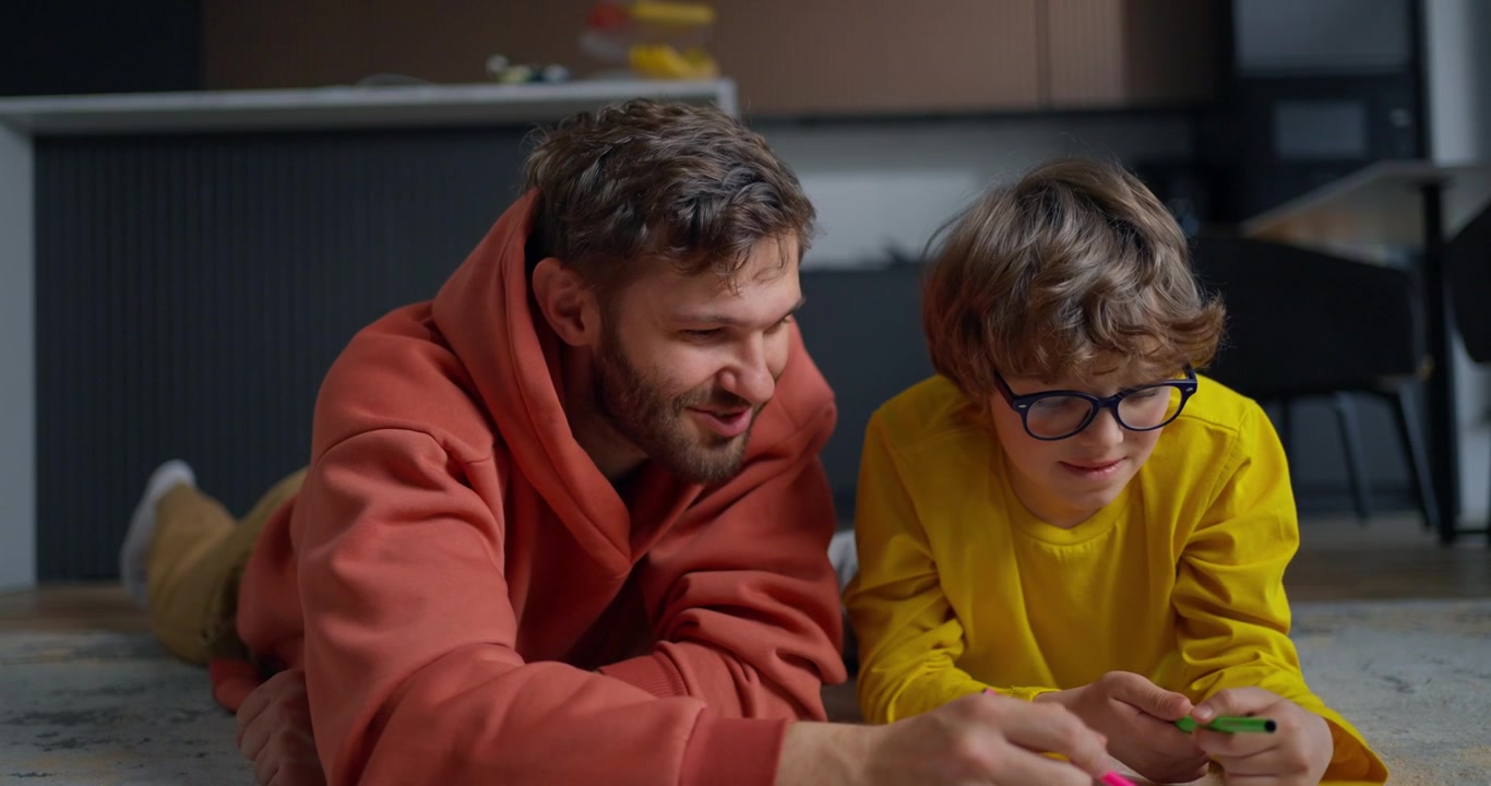 Padre e figlio felici che disegnano insieme sul pavimento a casa