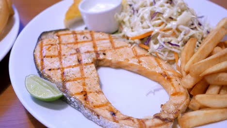 a plateful of flavourful food served in a restaurant, a combination of grilled salmon steak, french fries, and coleslaw salad