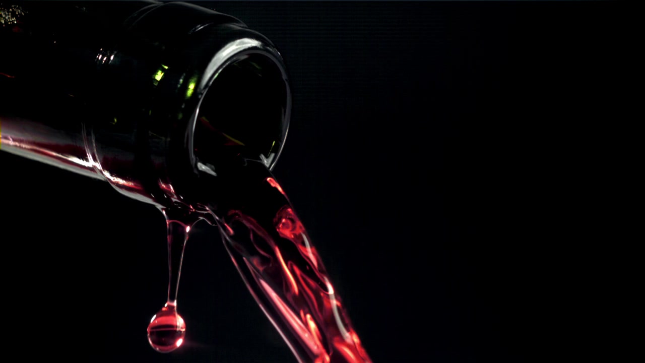 Versamento al rallentatore di vino rosso da una bottiglia su sfondo nero