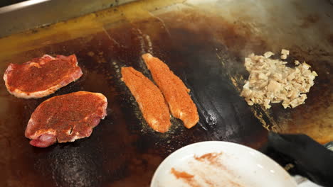 요리사는 돼지 갈비와 닭고기, 슬로우 모션 4k와 함께 지글거리는 평평한 상단 철판에 메기 필레를 놓습니다.