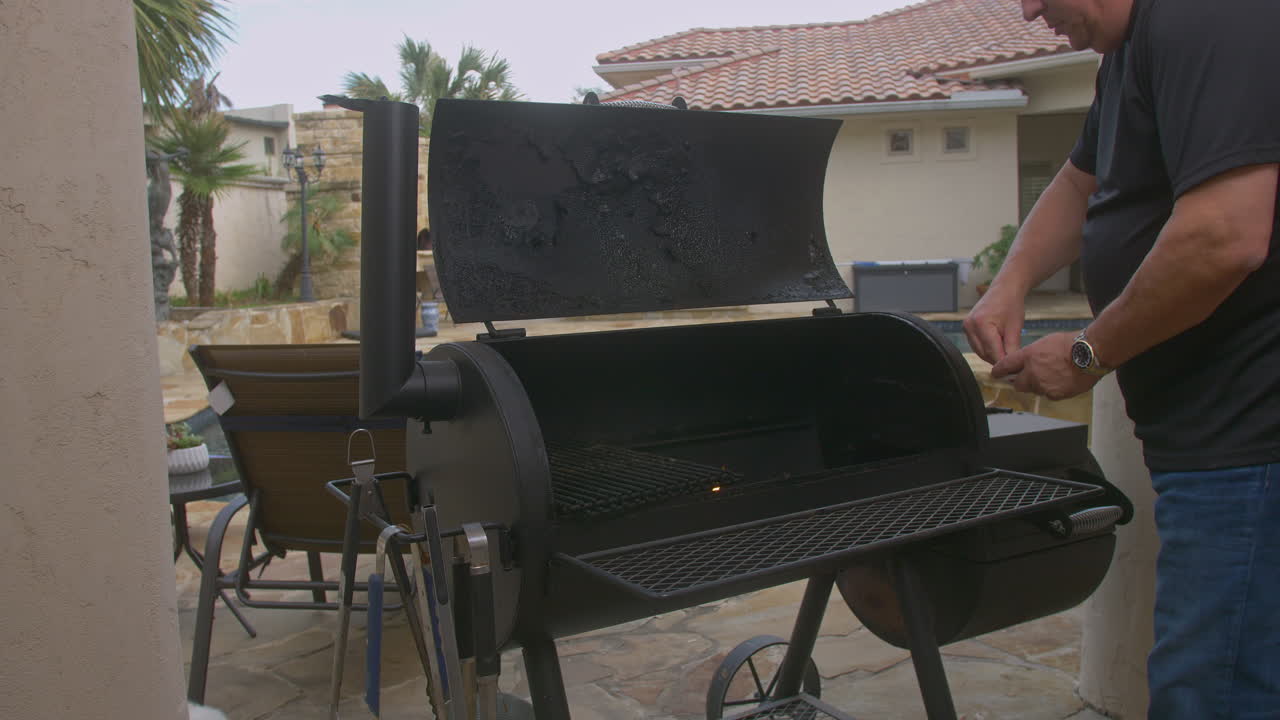 hombre luces coinciden y comienza el fuego en el pozo de barbacoa al lado de la piscina del patio trasero