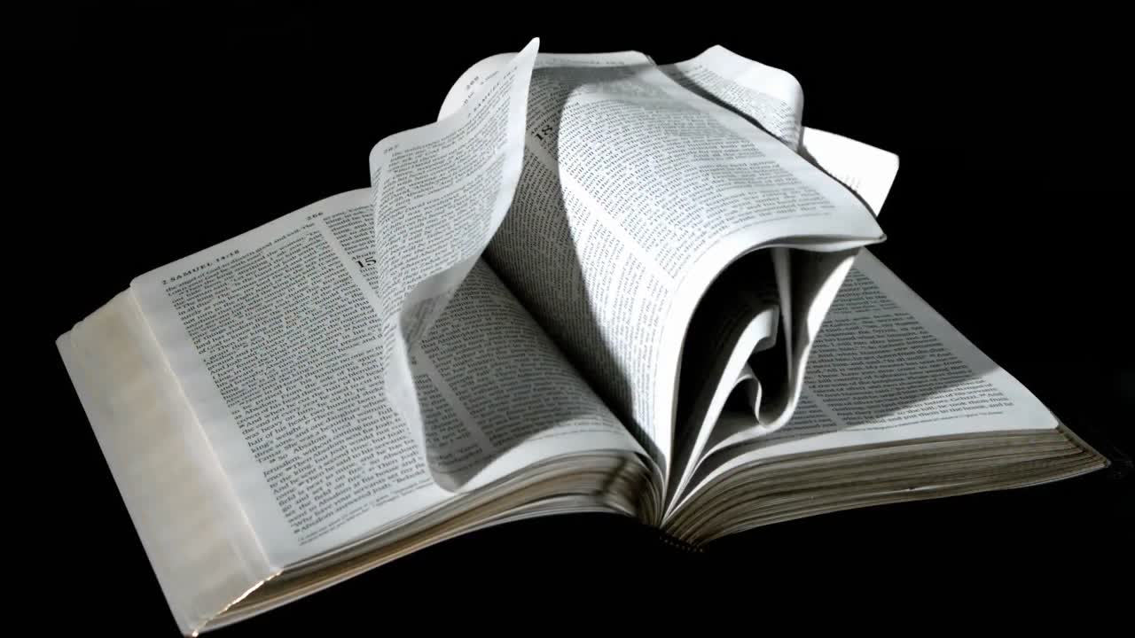 Bible pages turning in the wind on black background