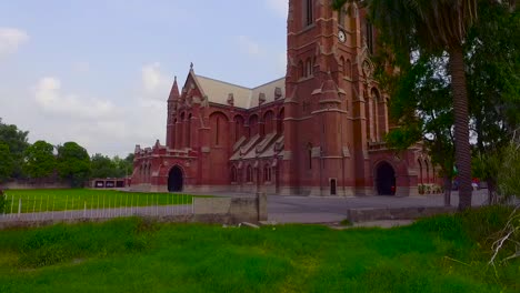 A-beautiful-old-Church-low-angle-view-by-drone,-Green-trees-and-grass-around-the-Church,-Two-cars-are-parked-in-the-parking