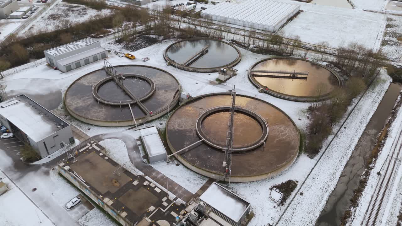 Top-down drone shot of a wastewater treatment facility with circular sedimentation tanks covered in snow, illustrating water management and environmental infrastructure