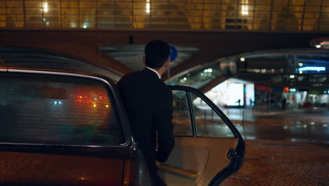 Businessman opening car door going into night street. Driver closed automobile