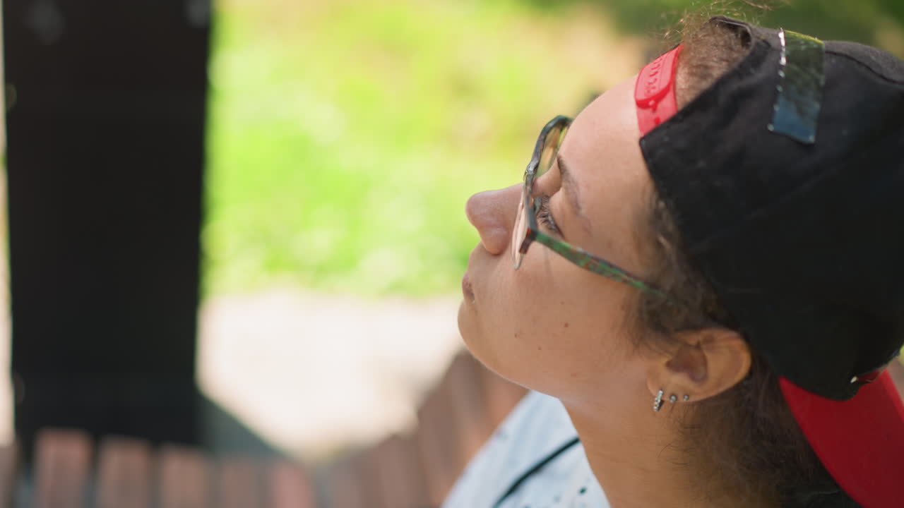 Youth rests outdoors, Youthful individual seated on wooden bench in tranquil park setting, Young adult takes creative break on wooden bench surrounded by lush greenery and warm sunlight