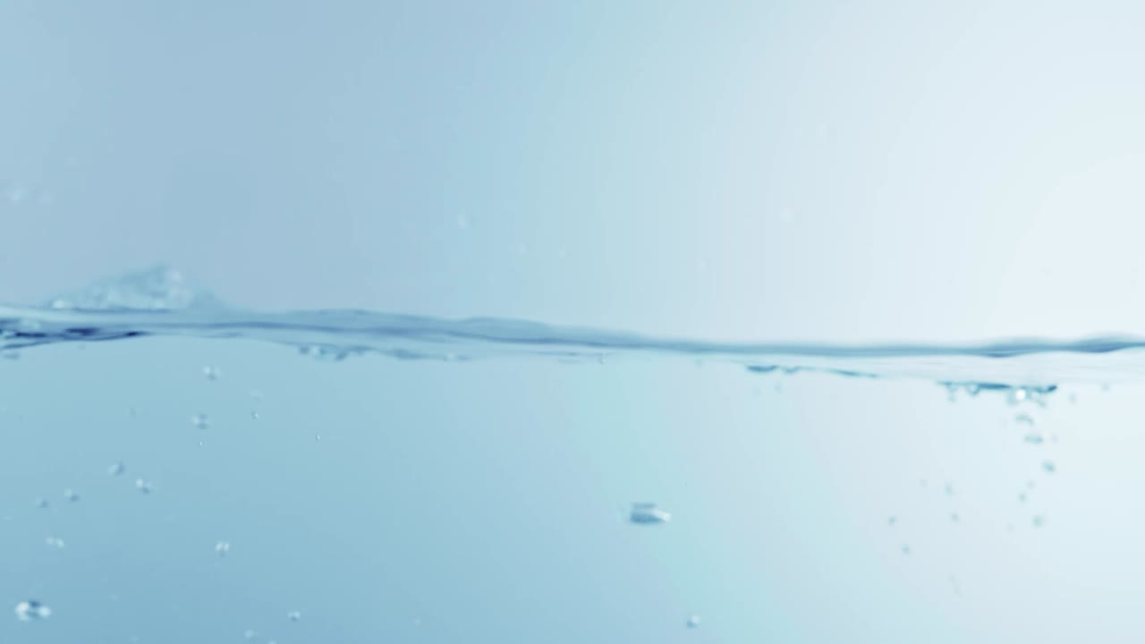 슬로우 모션의 깨끗한 물 표면은 물이 튀는 상점으로 화면을 채우고 기포로 액체 표면을 흔들고 있습니다.