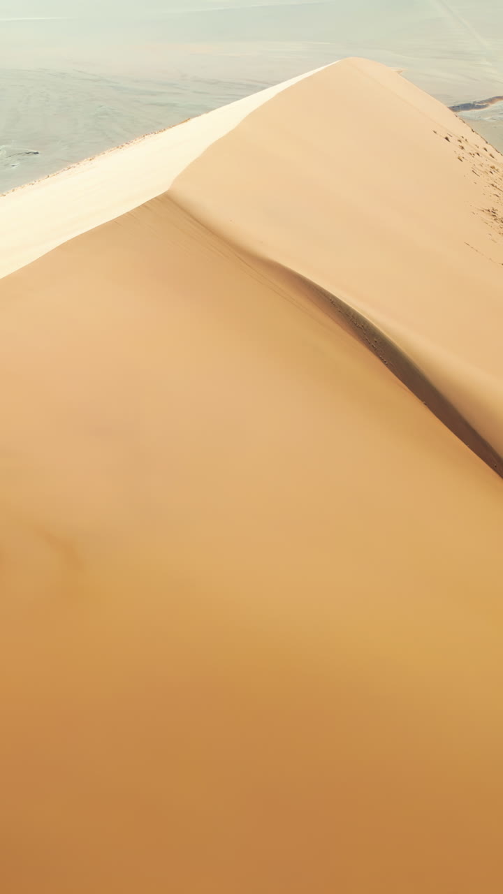 Vista aerea con drone lungo la cresta di un'imponente duna di sabbia nel deserto del Namib che evidenzia i motivi e le texture della sabbia modellati dal vento. Verticale.