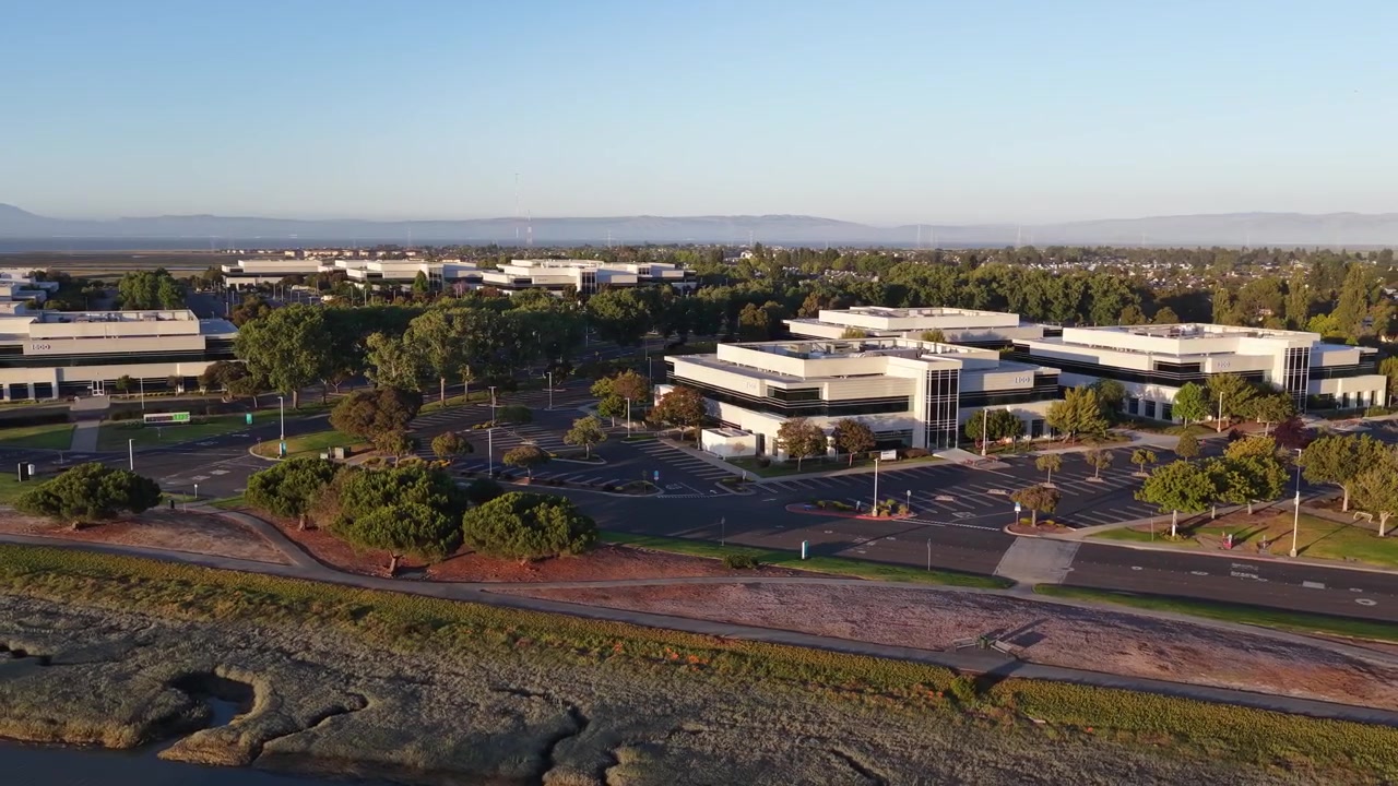 Riprese aeree con movimento laterale su un moderno parco commerciale a Redwood Shore, Redwood City, California, che mostrano edifici per uffici, parcheggi vuoti e un'area paludosa al tramonto.