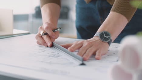 close up of male architect in office drawing on plan or blueprint with ruler