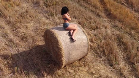 orbital shot of beautiful brunette woman sitting in bale of hay posing under the sun