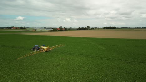 Vorbeifahrender-Traktor-Mit-Gezogener-Feldspritze-Auf-Einem-Bebauten-Feld,-Luftaufnahme