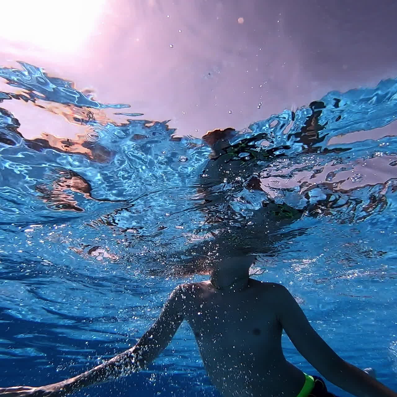 Underwater video of a boy swimming in blue clear water. Little boy dives under the water with closed eyes in the swimming pool.