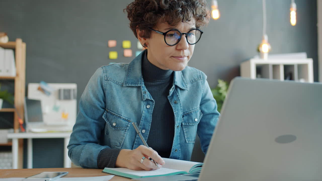 Woman Taking Notes on Laptop in Modern Office