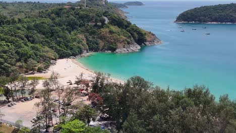 drone footage captures phuket's stunning coastline, featuring lush greenery, turquoise waters, and a serene temple under bright daylight