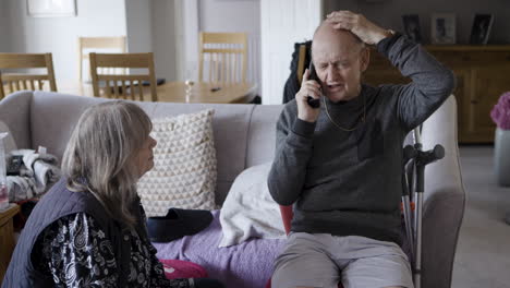 Older man talking on the phone with a woman beside him on the couch