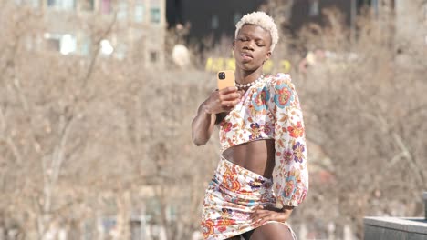 trendy black queer person in dress taking selfie on street