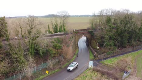 Drone-footage-showing-a-car-coming-under-a-railway-bridge-in-the-countryside