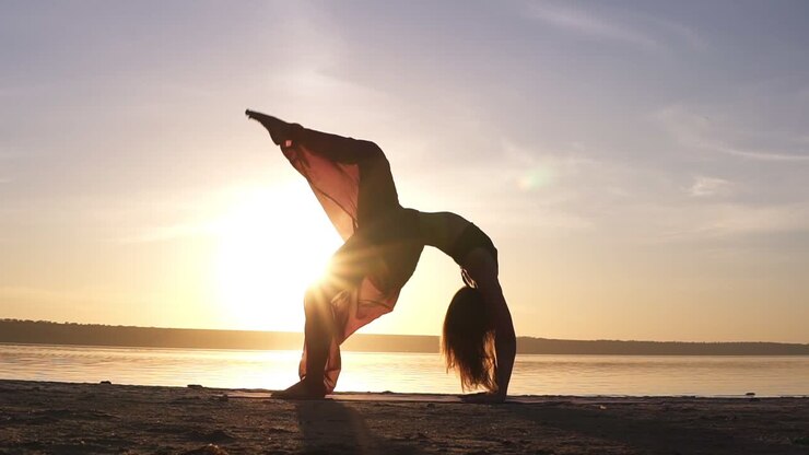 una giovane donna con bellissimi pantaloni da yoga colorati sta facendo un esercizio di yoga urdhva dhanurasana noto anche come postura di arco verso l'alto su una spiaggia vuota. luce solare sullo sfondo
