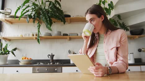 mujer transgénero caucásica no binaria que usa una tableta y bebe café en la cocina