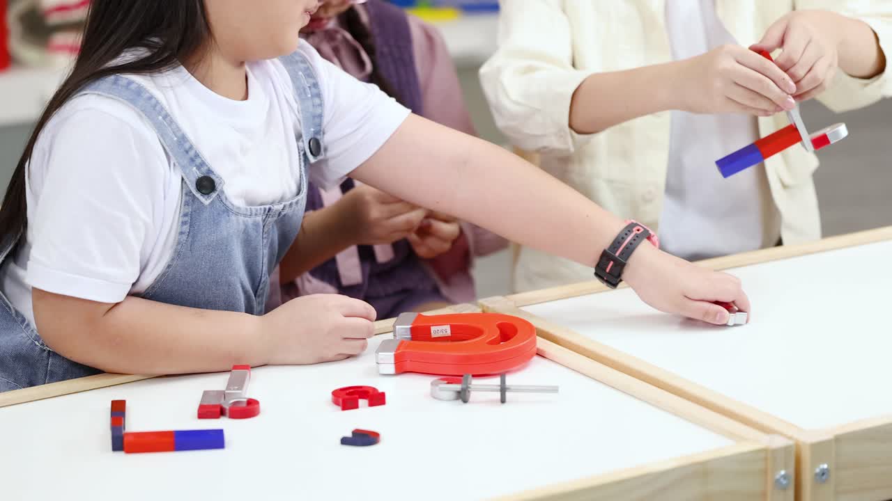Elementary students explore magnetic force with colorful magnets on classroom table, bright static camera shot