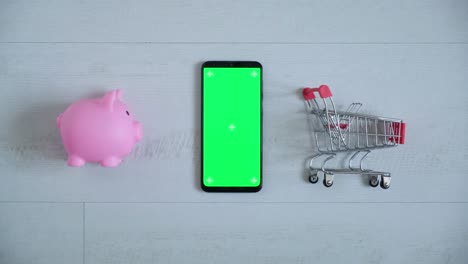 teléfono con una pantalla chromakey en las manos de un primer plano. vista superior de la caja de ahorros del teléfono inteligente y el carrito de compras copia el espacio sobre fondo blanco