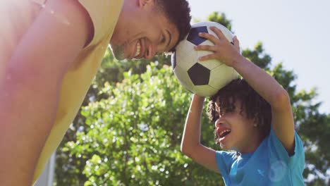 Happy-biracial-man-and-his-son-playing-football-in-garden