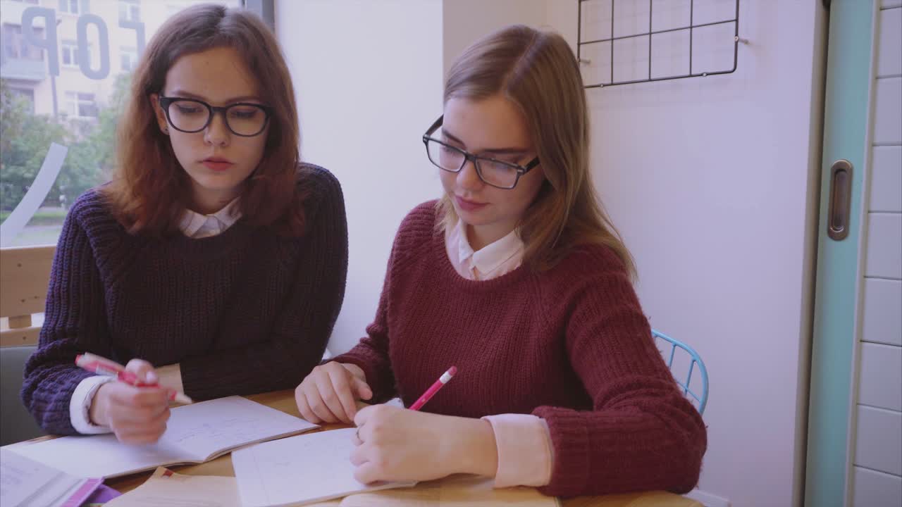 dos chicas estudiando juntas en una cafetería
