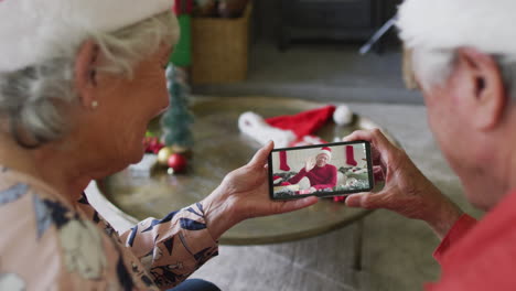 pareja caucásica mayor usando un teléfono inteligente para una videollamada de navidad con un hombre sonriente en la pantalla