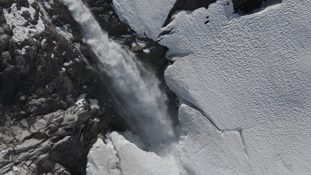 un avión no tripulado en cámara lenta volando alrededor de una poderosa cascada cerca del lago langvatnet en noruega cerca de strynefjellsveg rompiendo a través del hielo y la nieve en un día soleado rodeado de rocas brillantes