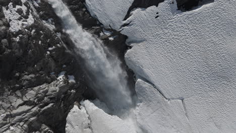 slowmotion drone shot flying around a powerfull waterfall near langvatnet lake in norway close to the strynefjellsveg breaking through ice and snow on a sunny day surrounded by shiny rocks log