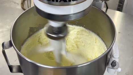 beating batter, cake mixtures in heavy duty electric mixer, tilt down close up shot at commercial kitchen setting