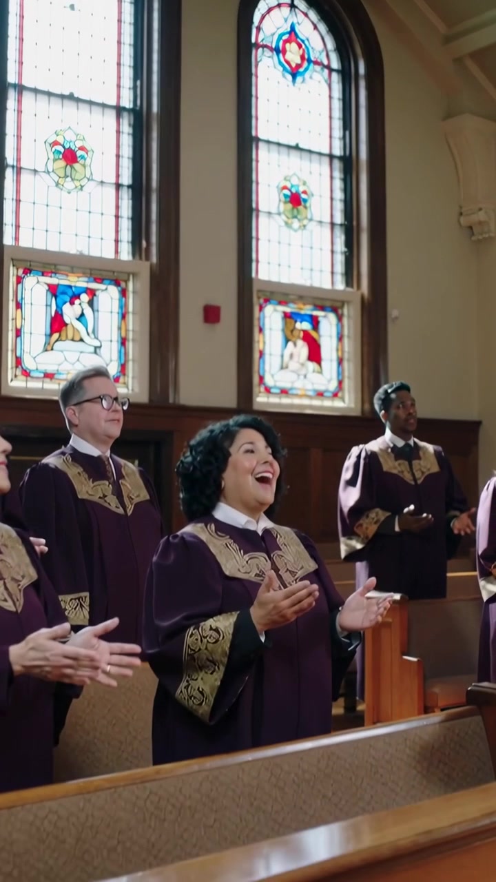 Vertical video: Singing woman in choir robe raising hands, hymn starting in church, stained windows