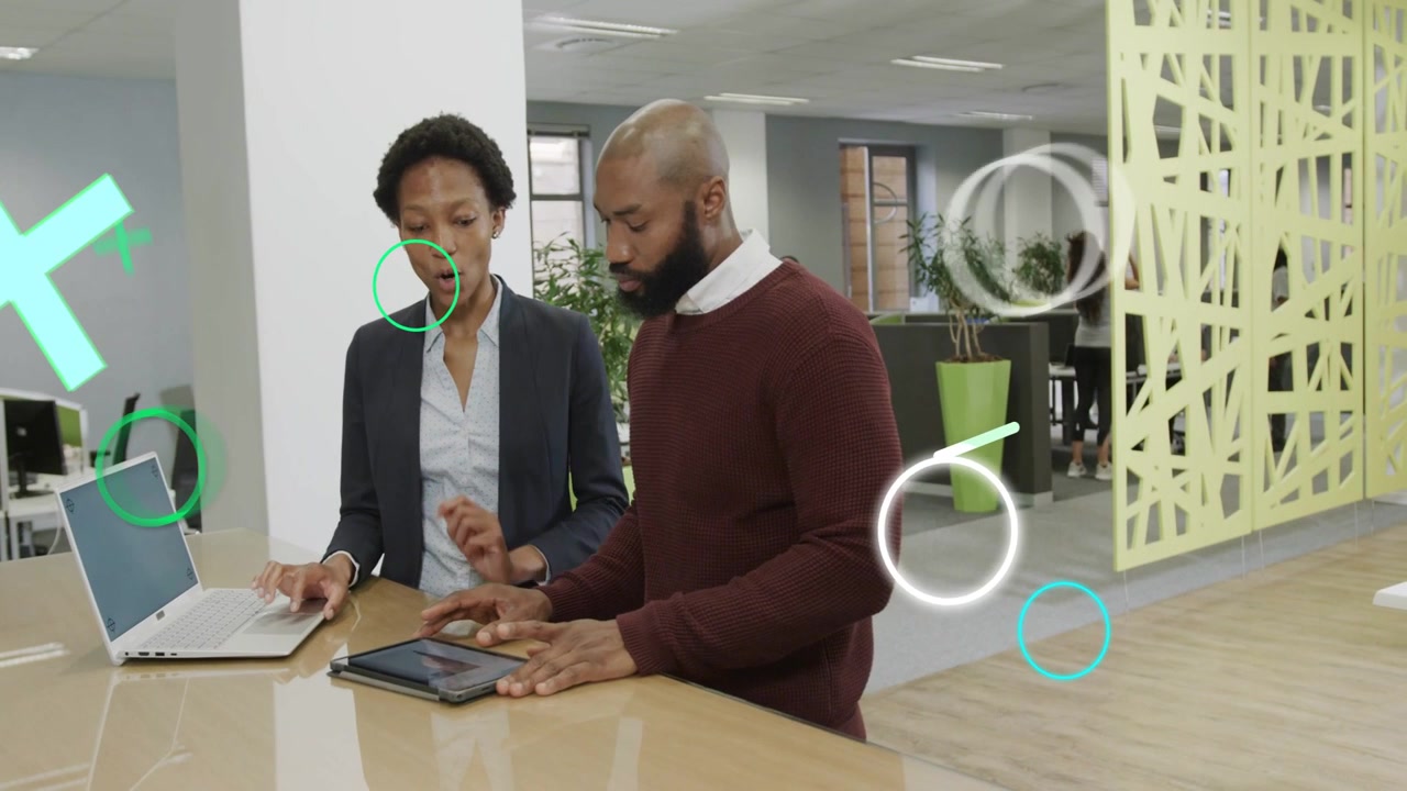 Business woman gesturing at laptop, leading man tapping tablet, green shapes flowing over frame