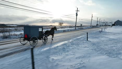 아미시 버기 (amisch buggy) 는 커스터 카운티 (lancaster county, pa) 의 눈 인 도로에서 해가 지는 하늘 아래