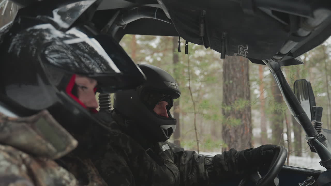 Primo piano di un pilota caucasico con casco che naviga con un ATV attraverso una pineta innevata, guida concentrata che controlla lo sterzo, mani guantate che stringono il volante, brina sulla visiera, roll-bar che incornicia l'abitacolo, inverno dalle luci soffuse