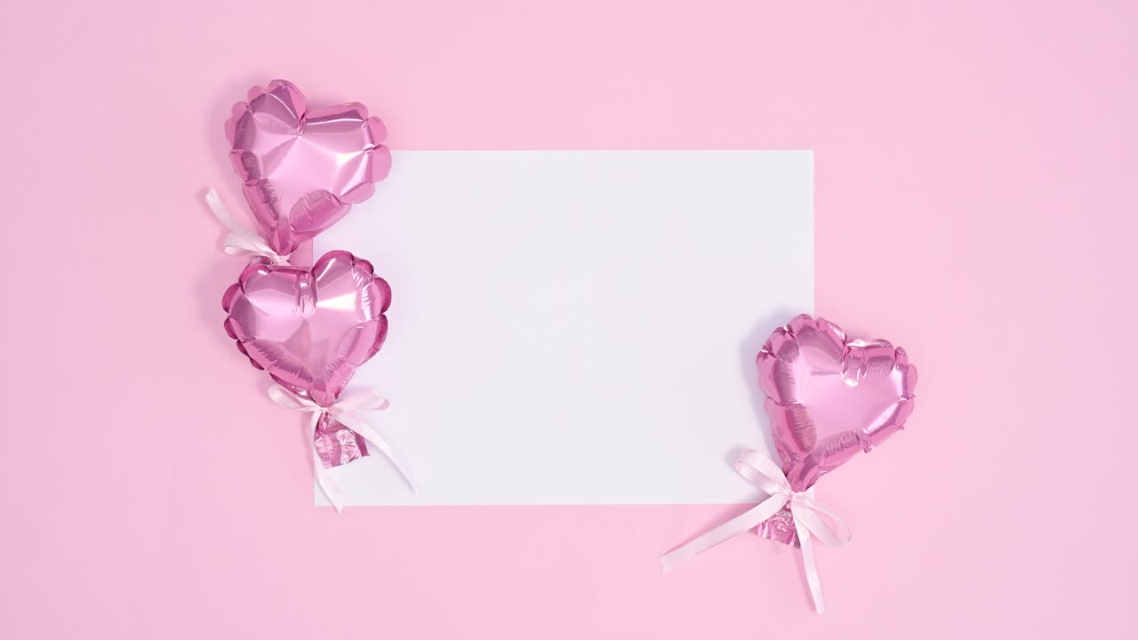 Piccoli e graziosi palloncini a forma di cuore rosa si muovono intorno a un biglietto di carta bianco per San Valentino. Animazione stop motion in flat lay.