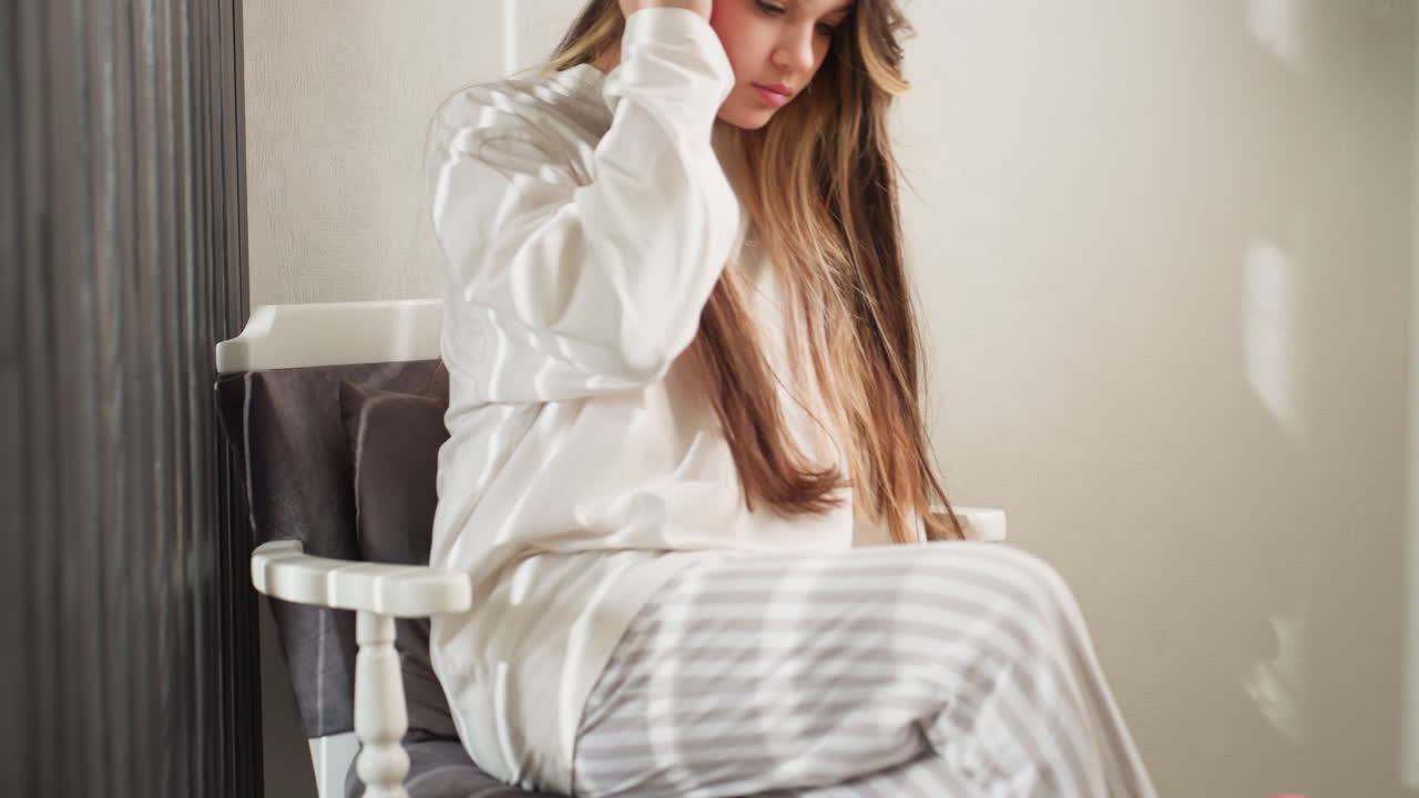 Schoolgirl walks to sofa in soft light and adjusts long hair then reaches for black nail polish on table with motion curtain background indoor mood blur steps before sitting to begin manicure
