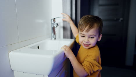 smiling caucasian baby in the bathroom. kid is happy to open and close the water tap.
