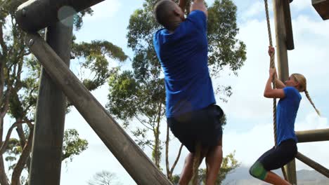 Fit-man-and-woman-climbing-rope-during-obstacle-course